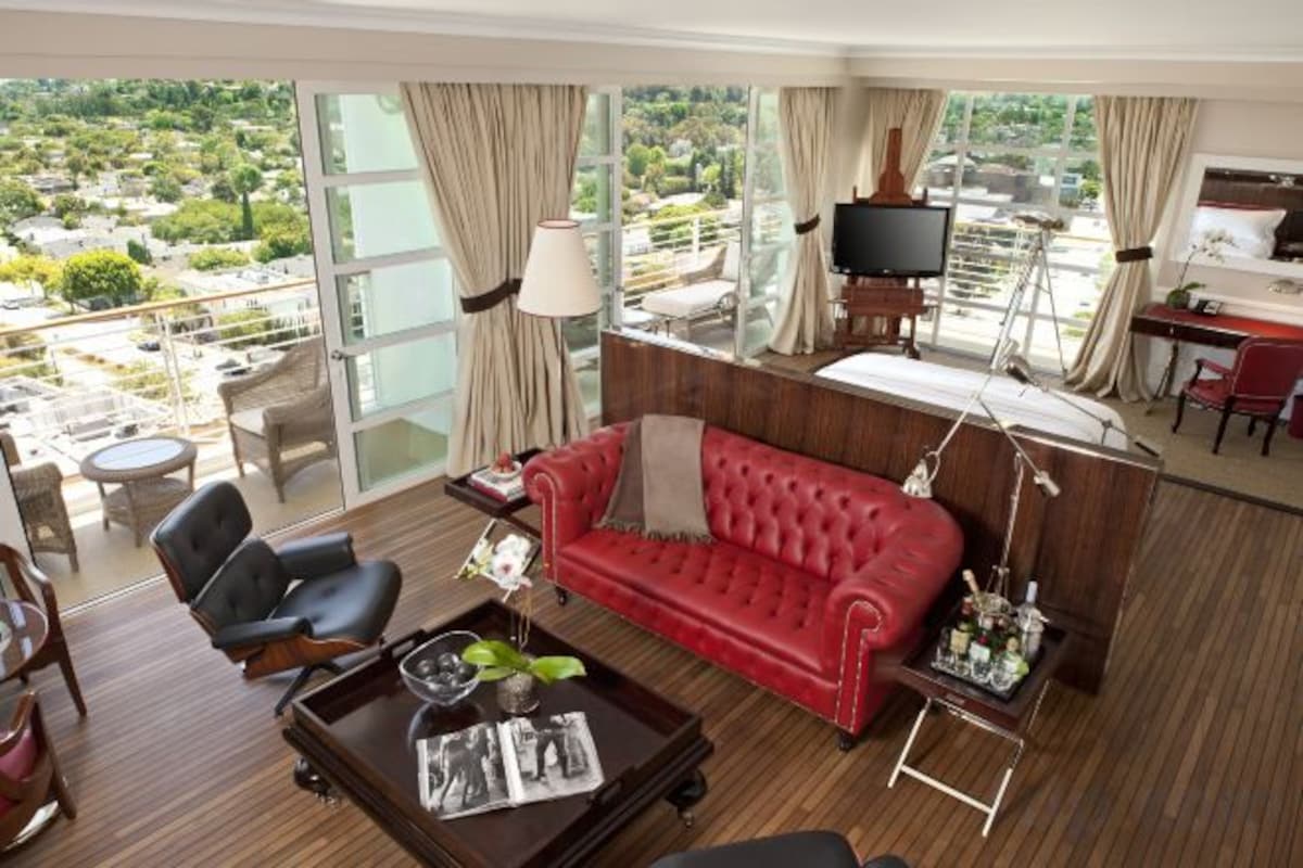 A hotel room with a red sofa, a TV, a balcony with a view, and a desk with a chair.