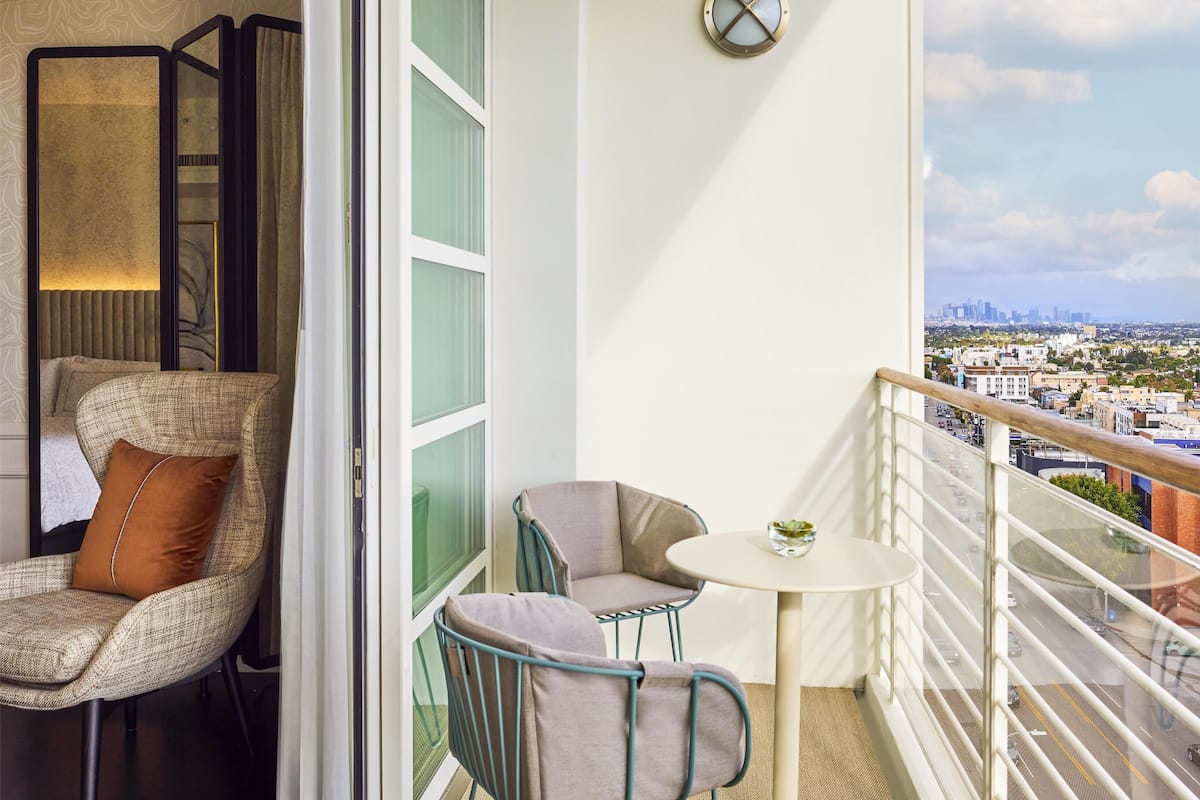 A balcony with a city view, a chair, a table, and a decorative wall piece.