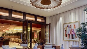 A spacious dining area with wooden tables and chairs, a large hanging light fixture, and a view into the adjacent bar area. - Cameo Beverly Hills, LXR Hotels & Resorts (Los Angeles)