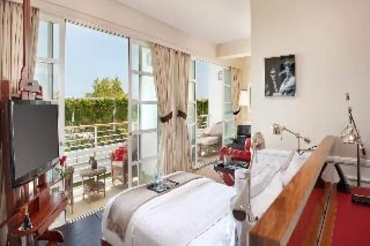 A hotel room with a bed, a desk, a chair, a TV, and a balcony with a view.