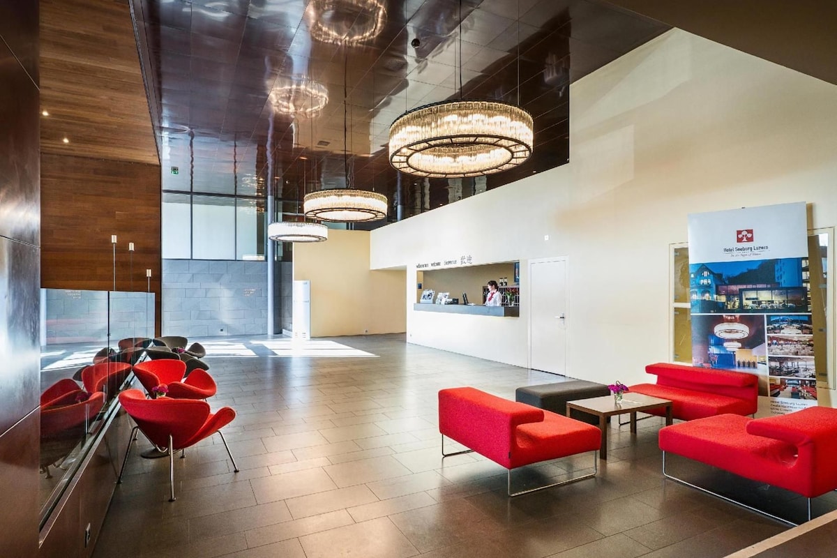 A modern lobby with red seating, a reception desk, and a large chandelier.