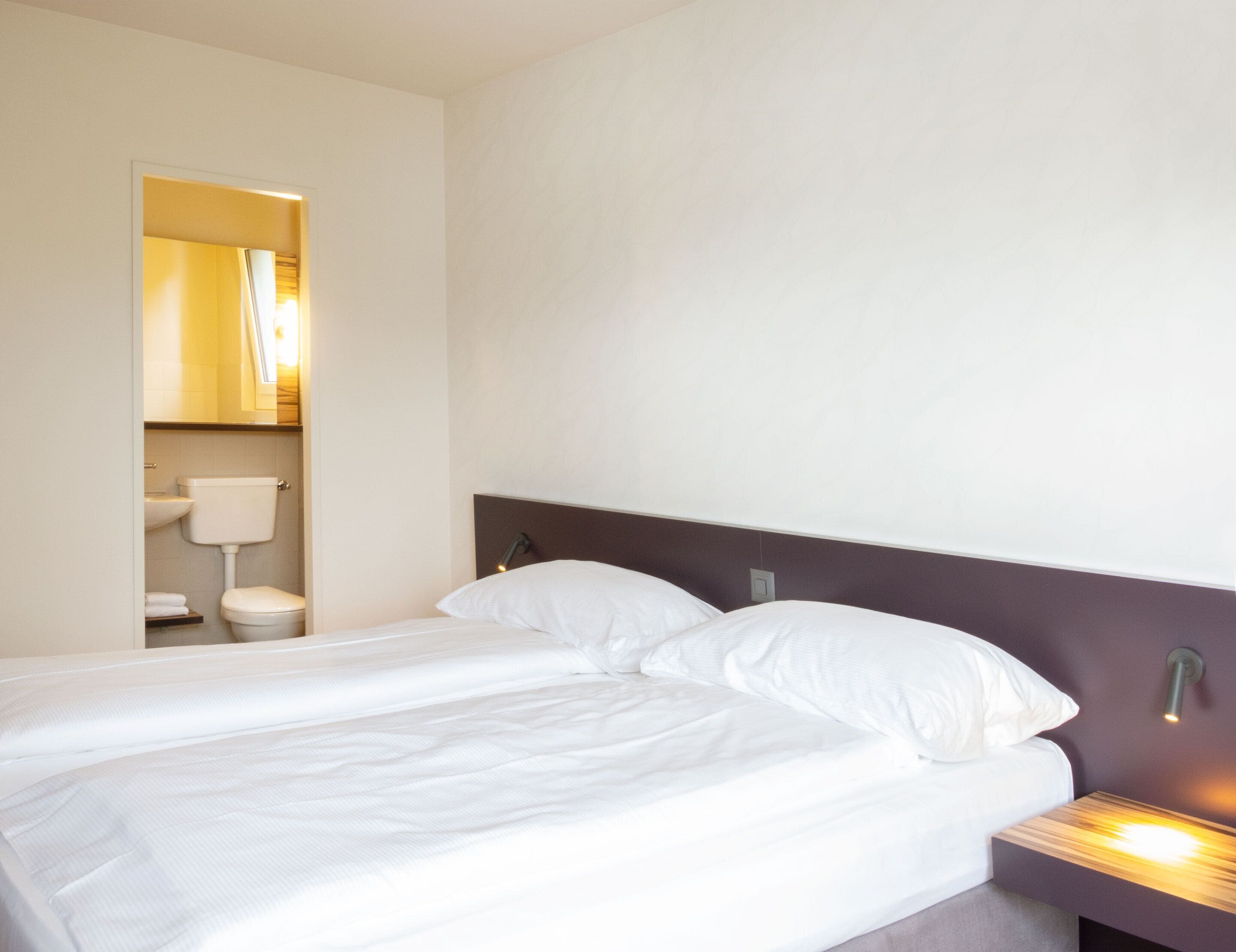 Habitación de hotel con una cama, una mesita de noche y un baño visible a través de una puerta abierta.