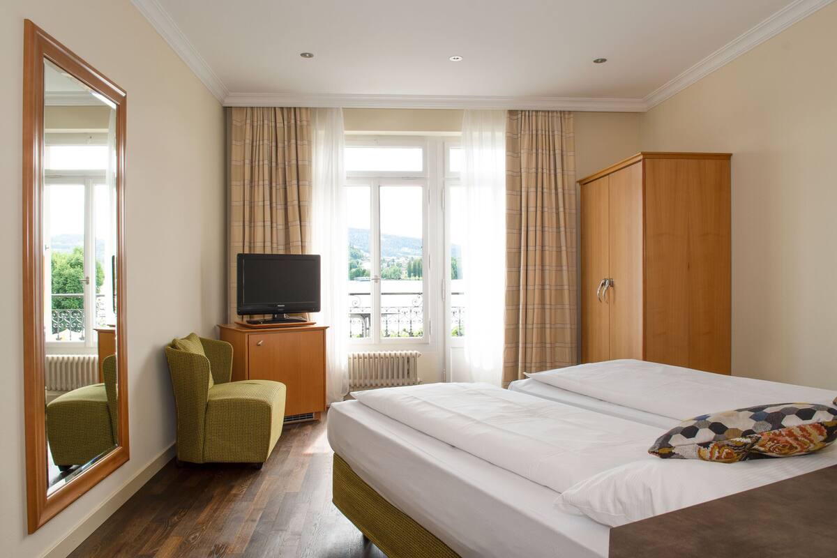 A hotel room with a bed, a television on a wooden cabinet, a green armchair, and a wardrobe.