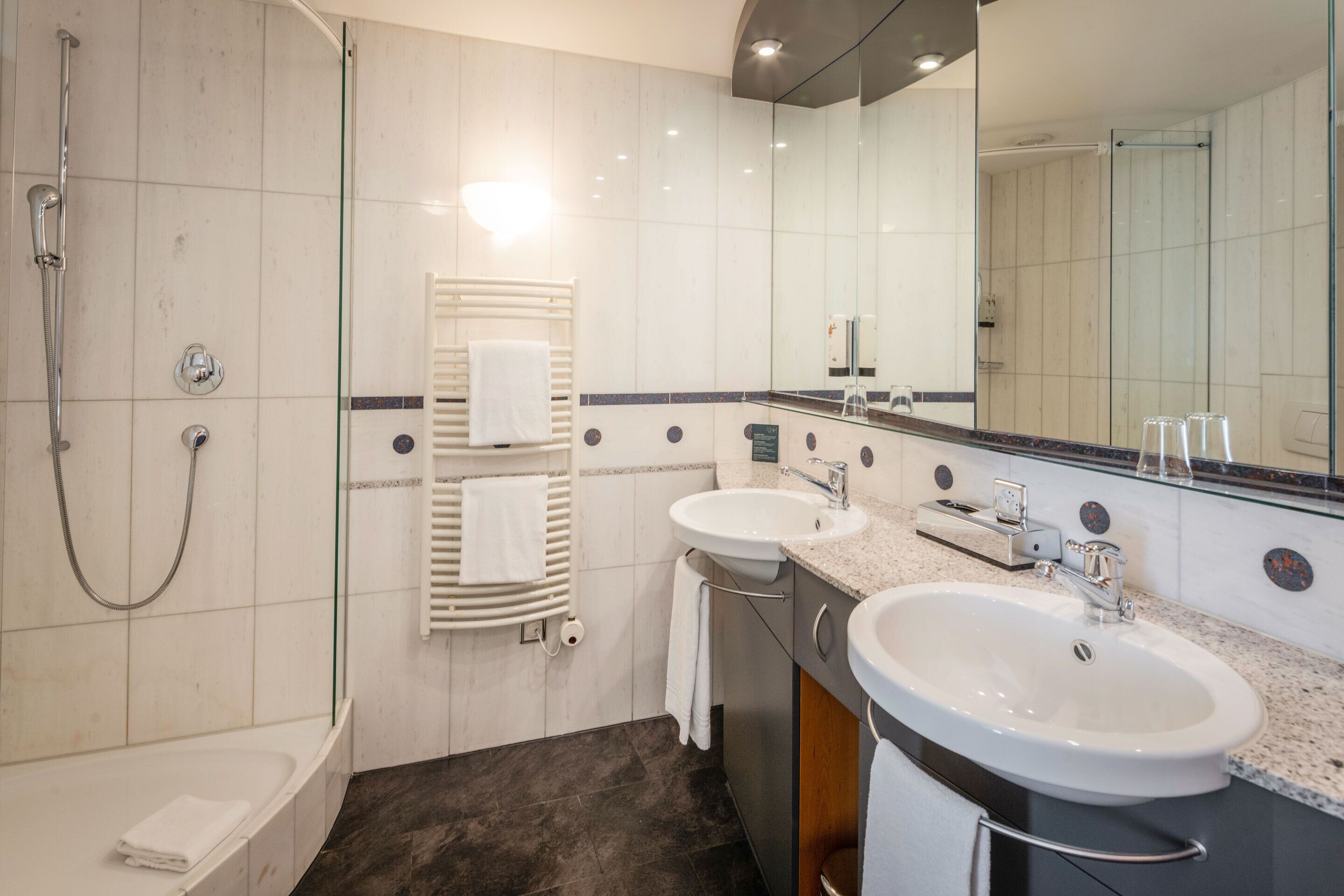 A modern bathroom with a bathtub, two sinks, a glass shower enclosure, and a large mirror.