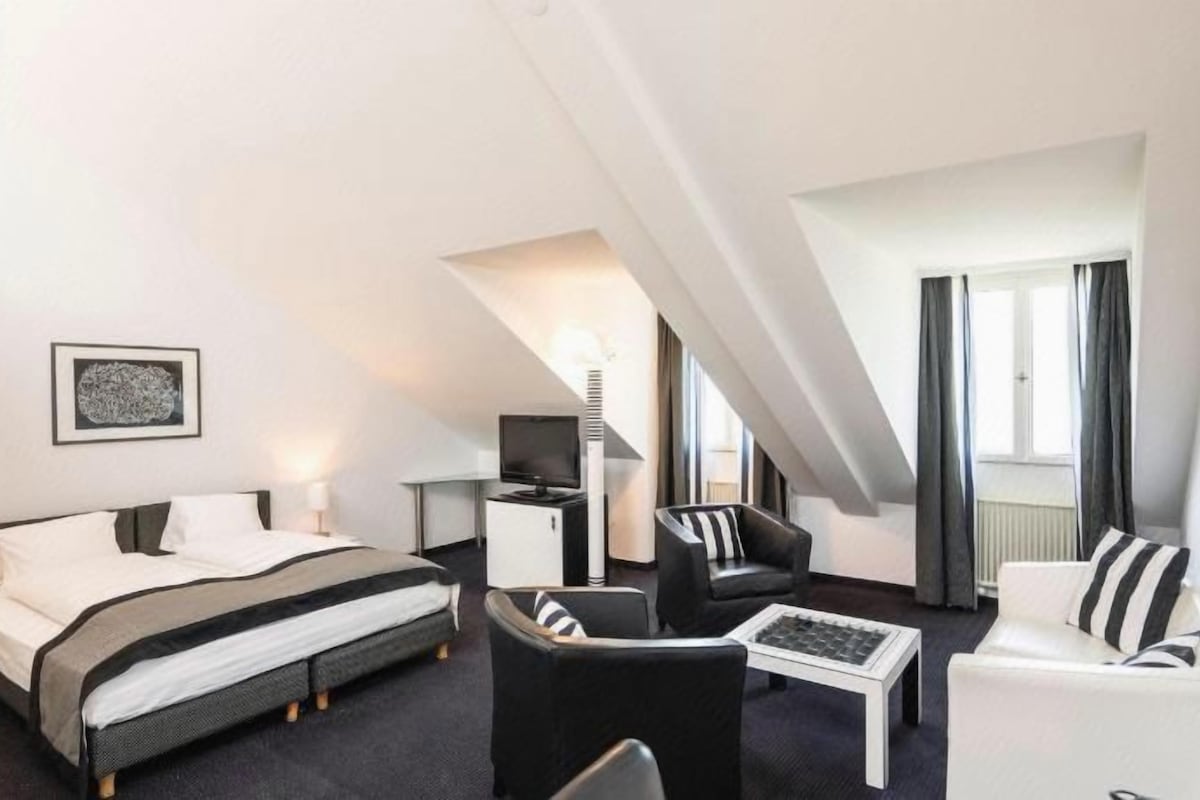 A modern hotel room with a bed, a desk, a chair, and a sofa.