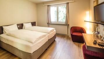 Una habitación de hotel con cama doble, un sillón rojo, una mesa de madera con un control remoto y un televisor.