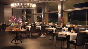A restaurant interior with round tables, chairs, and large circular chandeliers. - Seeburg Hotel (Lucerne)