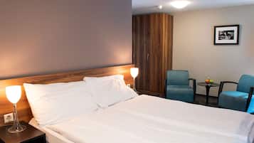 Habitación de hotel con una cama grande, dos lámparas de noche, un armario de madera, una pequeña mesa con fruta y dos sillas azules.