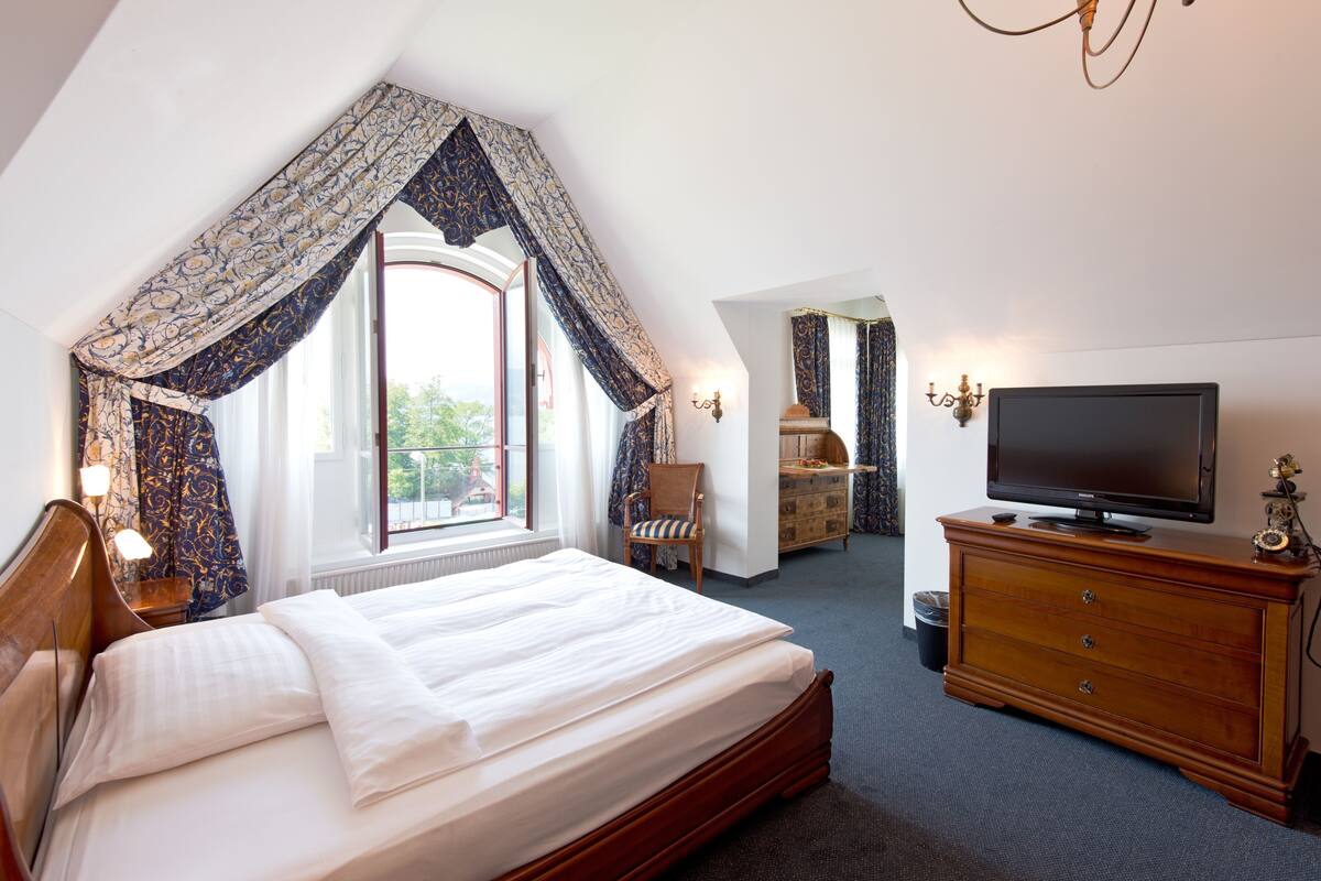 A hotel room with a large bed, a TV, a dresser, and a window with curtains.