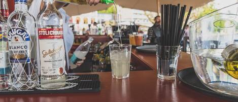 A bar area with various bottles of alcohol, a glass of water, and a tray with black straws.