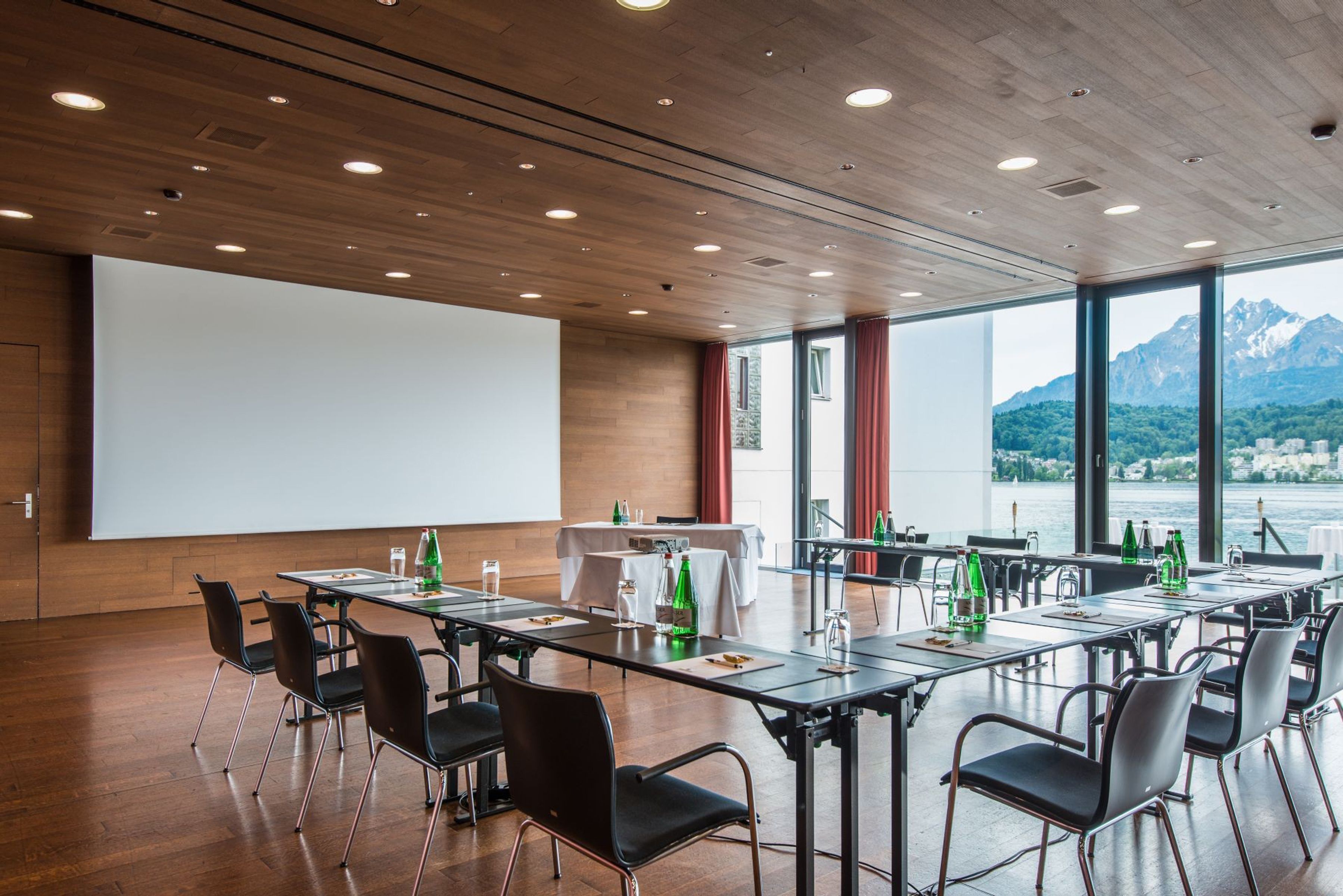 A conference room with a large projection screen, tables with chairs, and a view of mountains through large windows.