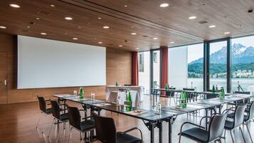 A conference room with a large projection screen, tables with chairs, and a view of mountains through large windows.