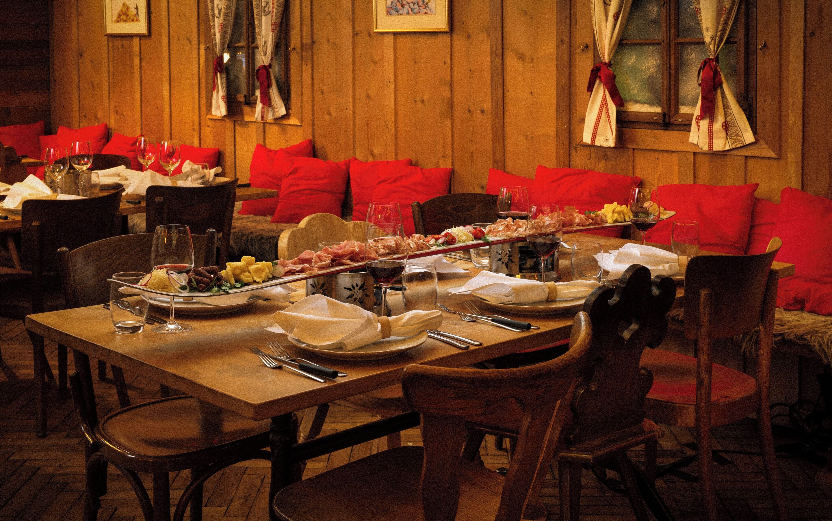 A wooden interior with red upholstered seating, a long dining table set with plates, glasses, and cutlery.