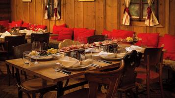 A wooden interior with red upholstered seating, a long dining table set with plates, glasses, and cutlery.
