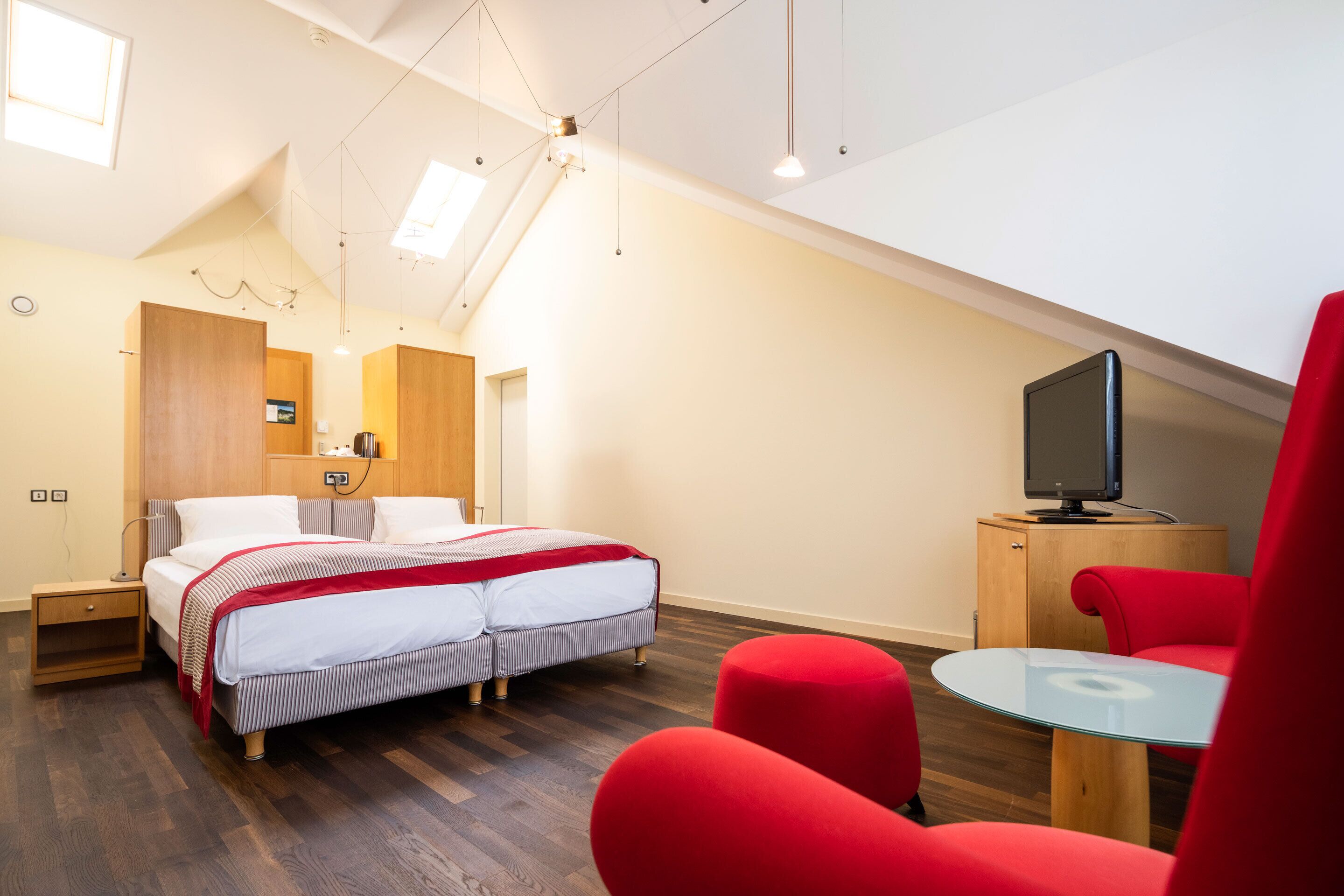 Un dormitorio moderno con cama, televisión y sillas rojas.