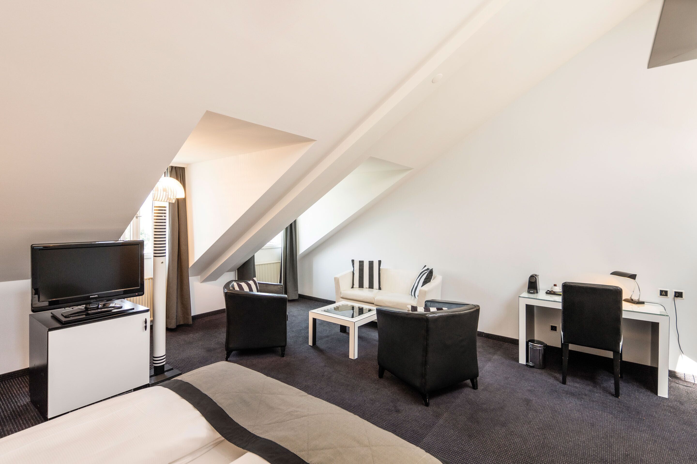 Una habitación de hotel moderna con cama, escritorio, sillón, sofá, televisor y lámpara.