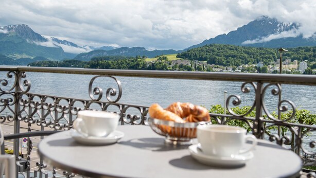 A table with two cups and a bowl of croissants, overlooking a lake and mountains. - Seeburg Hotel (Lucerne)