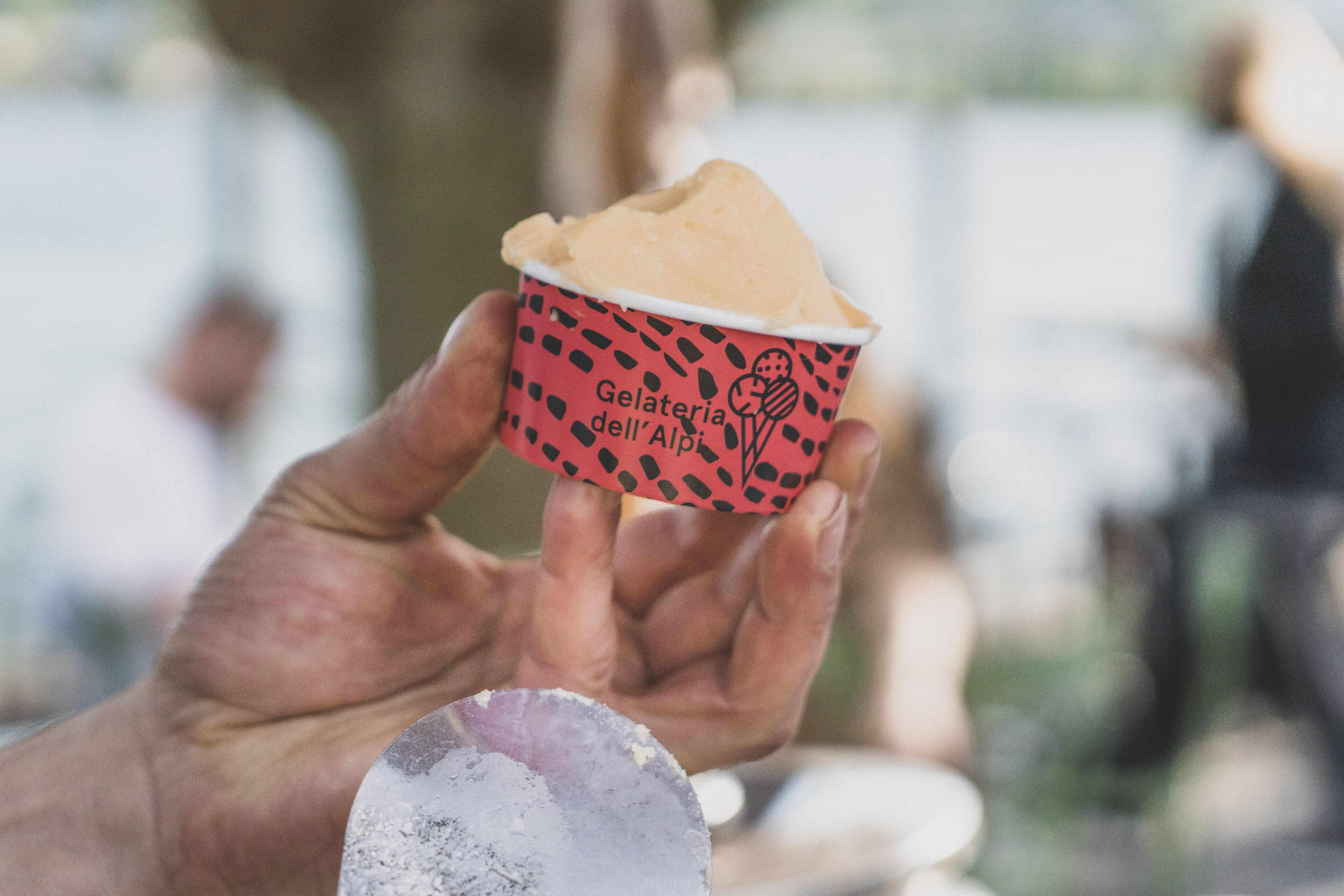 Una mano sosteniendo un vaso de helado con una tapa de diseño rojo y negro.