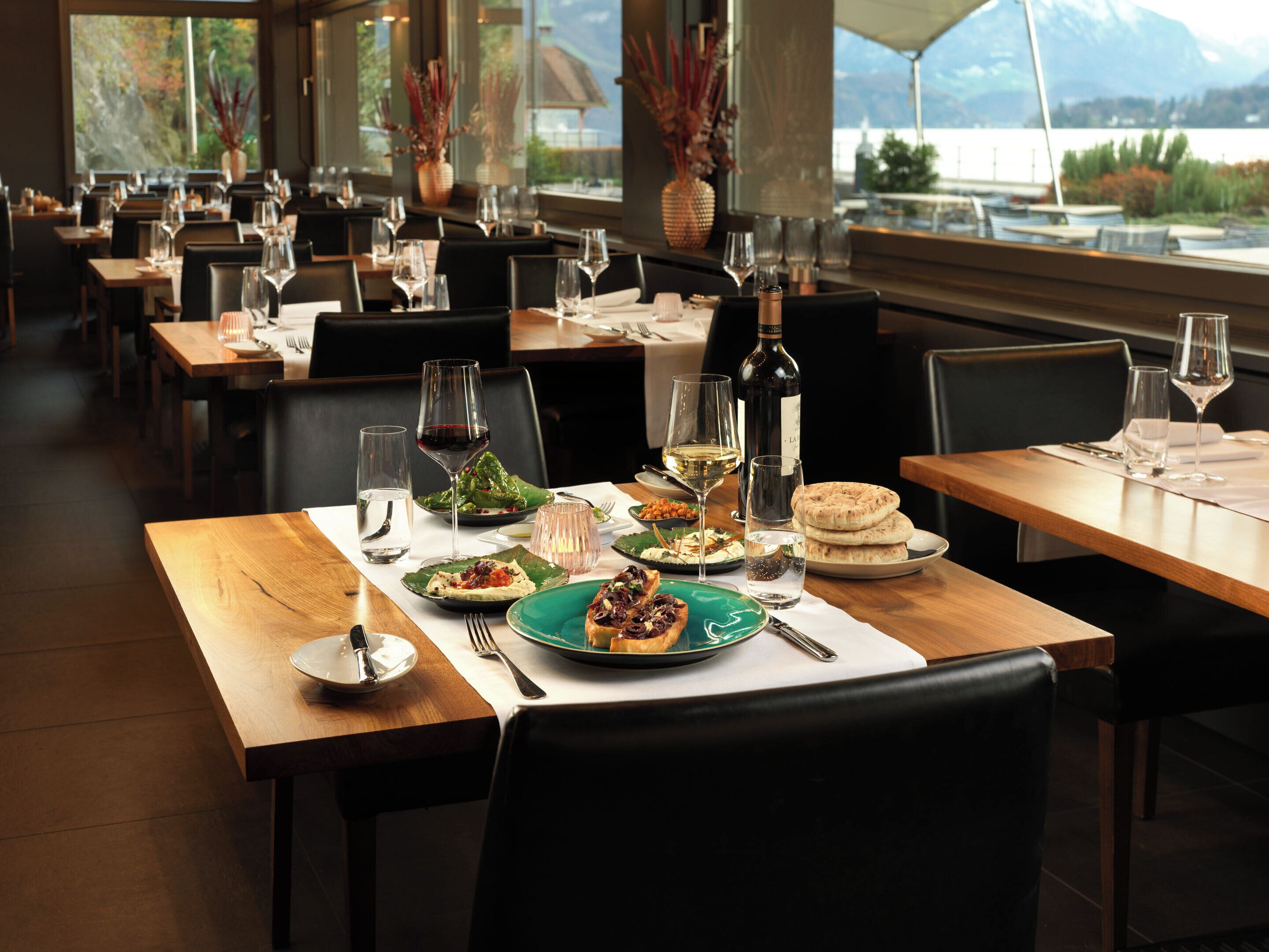 A restaurant with multiple tables set for dining, featuring a variety of dishes and wine glasses.
