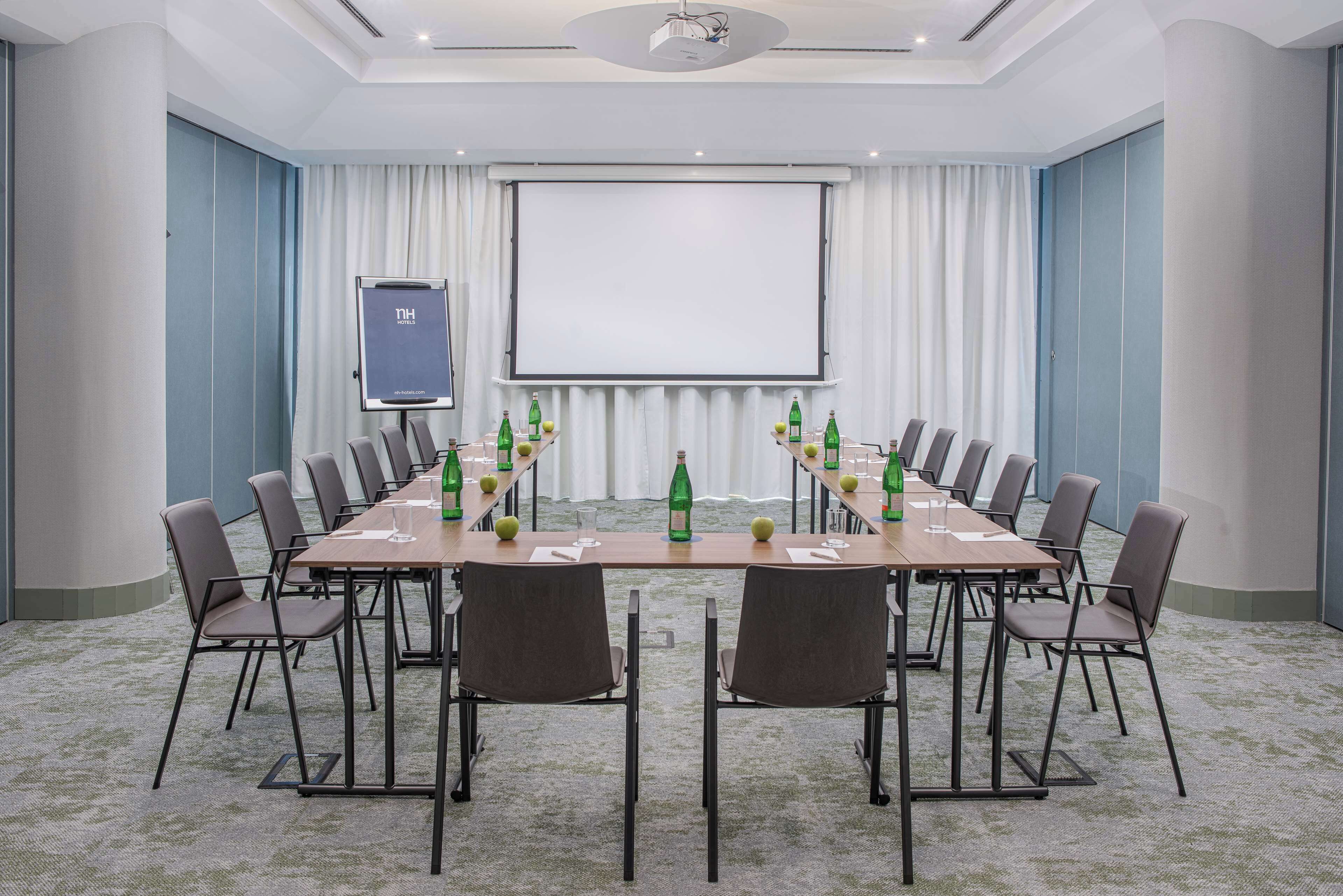 Ein Konferenzraum mit einem langen Tisch, Stühlen, einer Projektionsleinwand und Wasserflaschen.