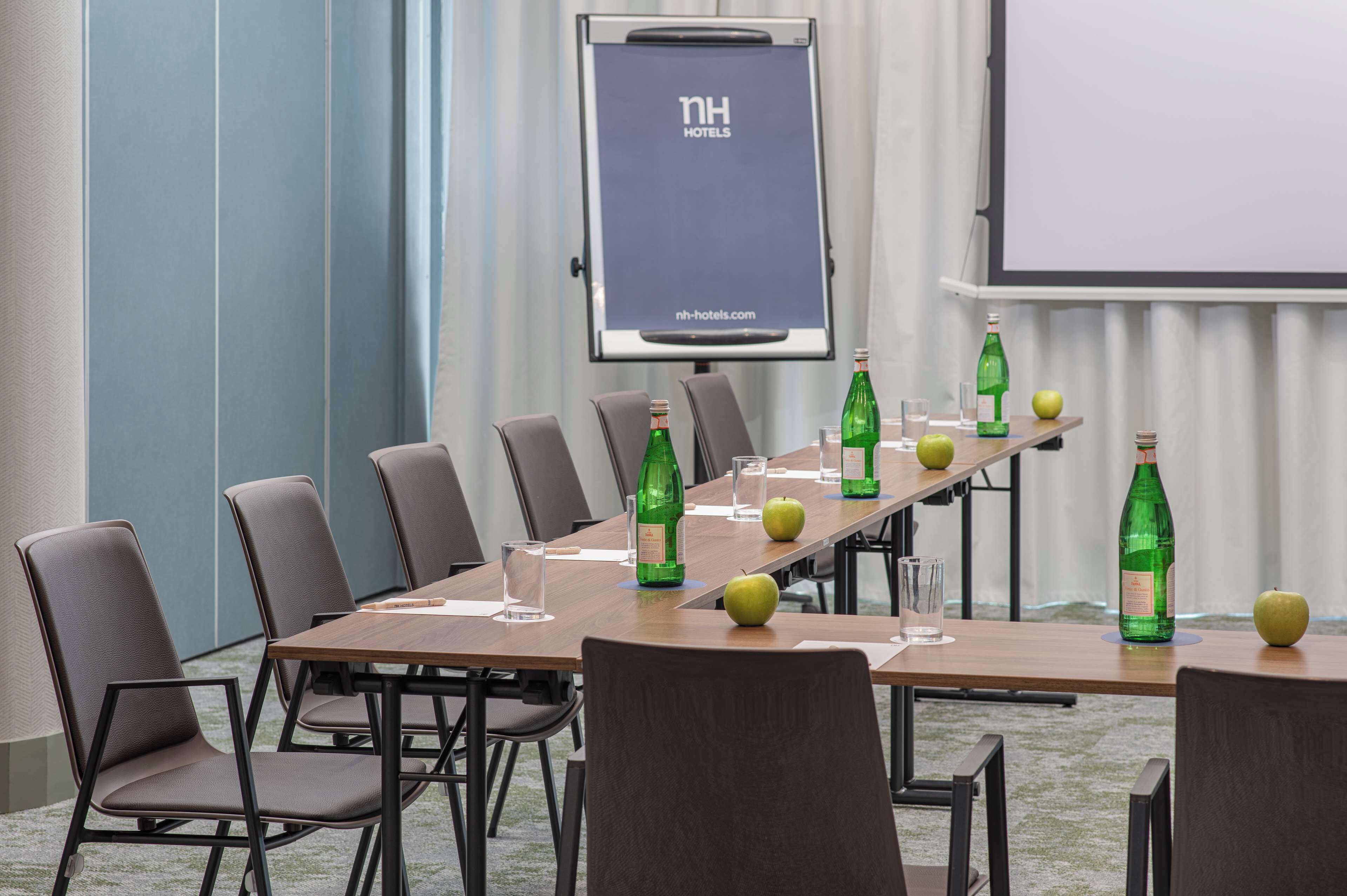 Une salle de conférence avec une longue table, des chaises, un écran de projection, ainsi que des bouteilles vertes et des pommes.