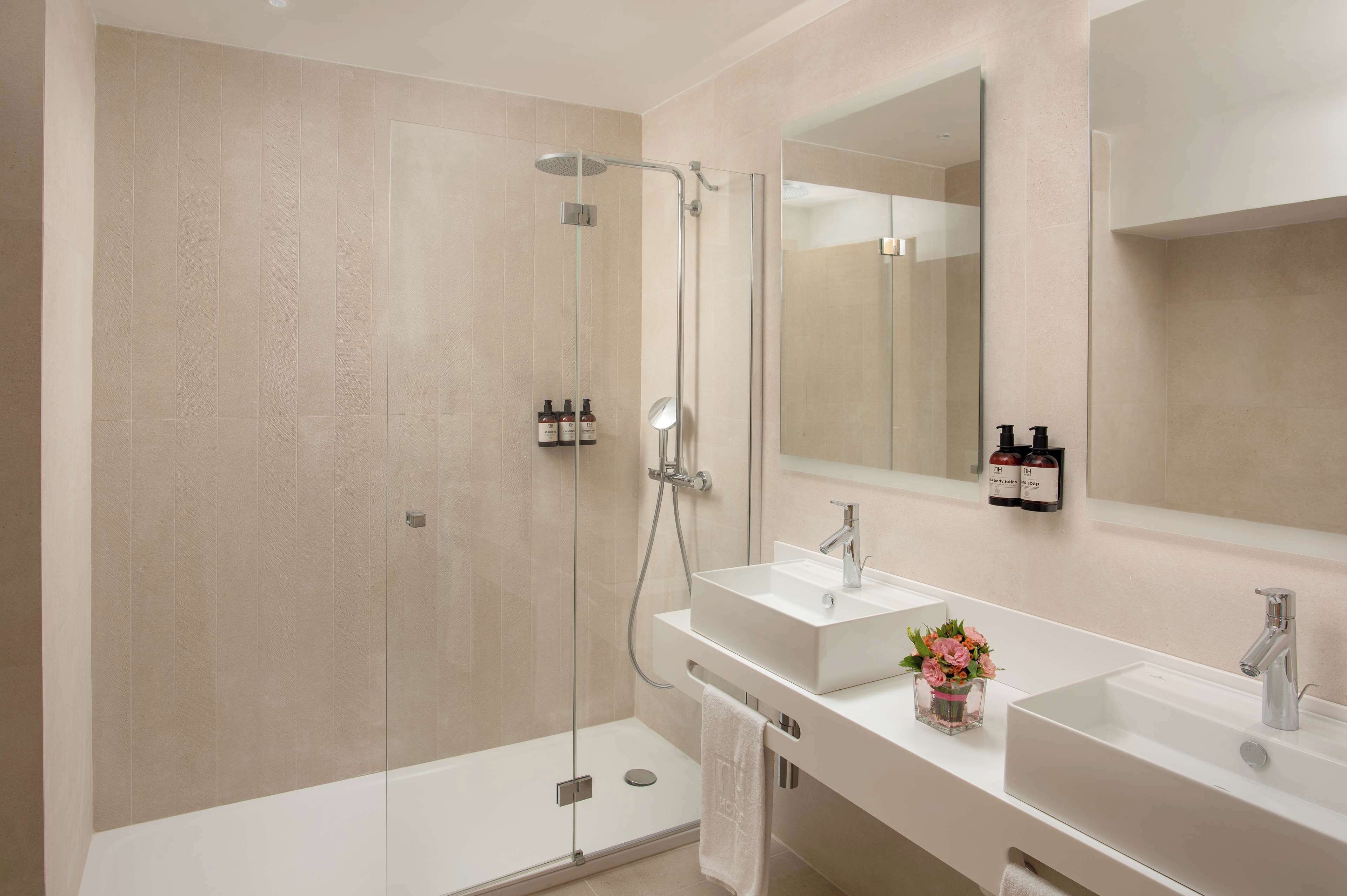 A modern bathroom with a glass-enclosed shower, two sinks, a large mirror, and toiletries on the wall.