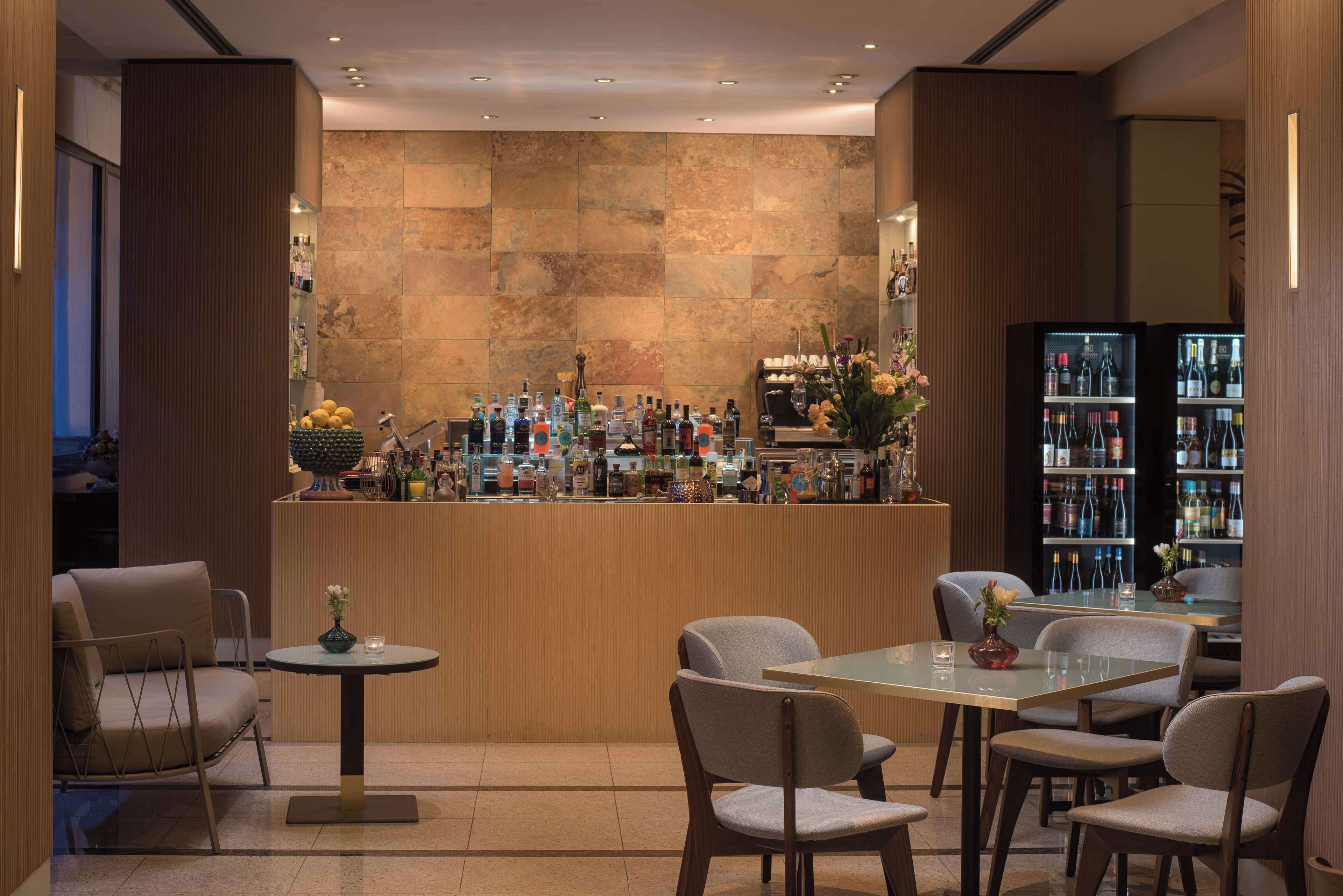 A bar area with a variety of bottles and a selection of flowers. There are several chairs and a table in the foreground.