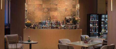A bar area with a variety of bottles and a selection of flowers. There are several chairs and a table in the foreground.