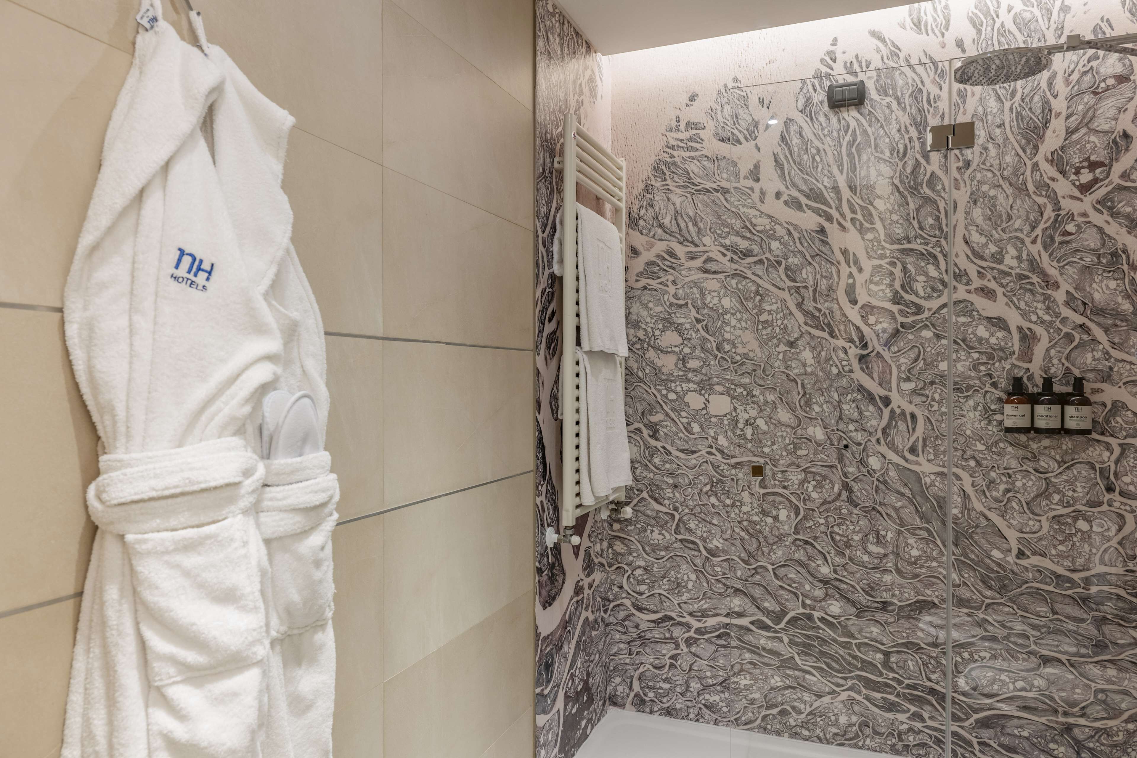 A bathroom with a white robe hanging on a rack, a shower with a marble wall, and a towel rack with multiple towels.