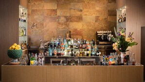 A bar area with a variety of bottles and glasses, a fruit bowl, and a vase with flowers. - NH Catania Centro (Catania)