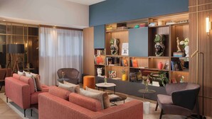 A modern living room with a sectional sofa, a small round table, and a bookshelf filled with books and decorative items. - NH Catania Centro (Catania)