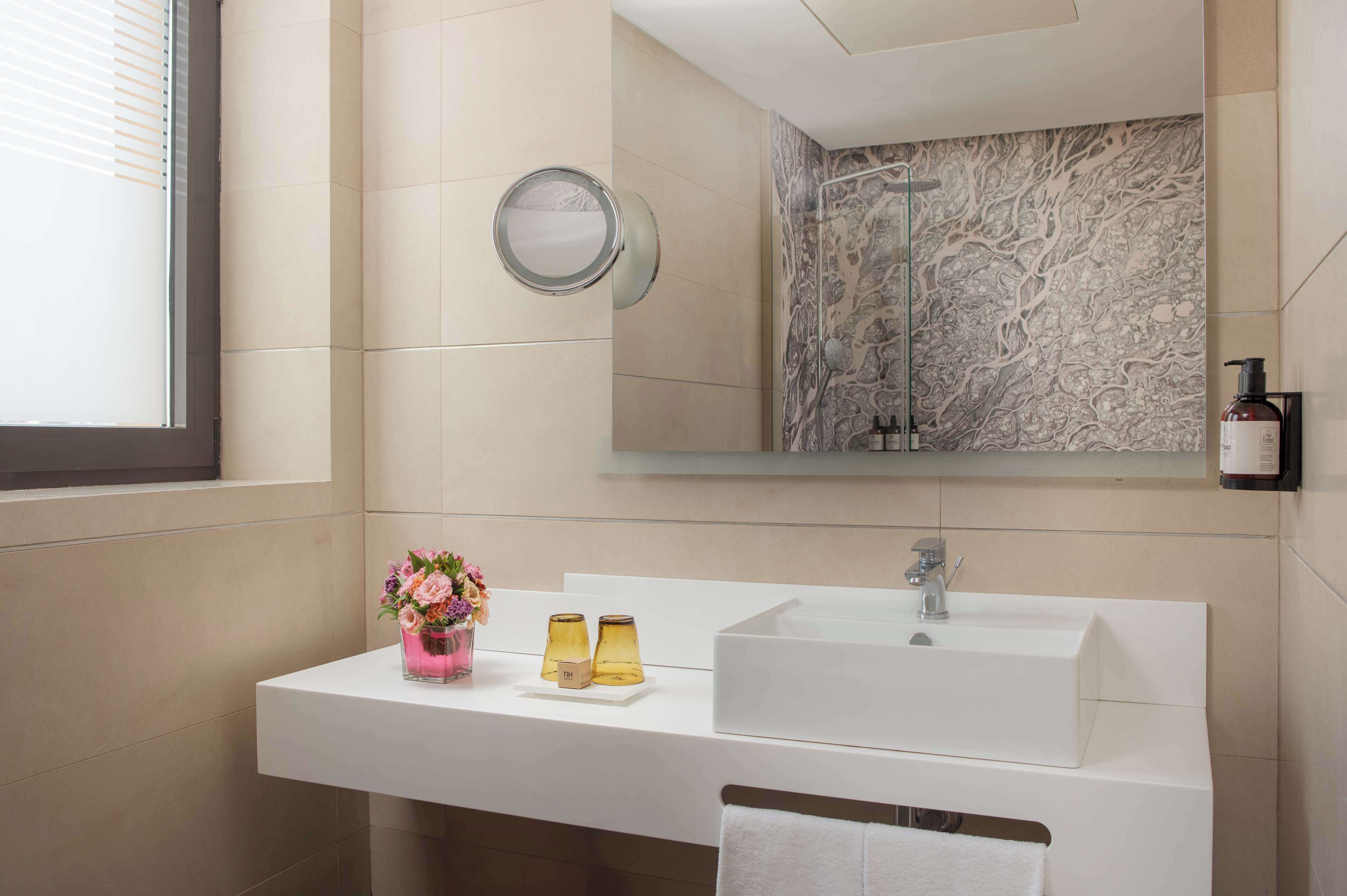 Un baño moderno con un lavamanos blanco, un espejo grande y una ducha con pared de mármol.