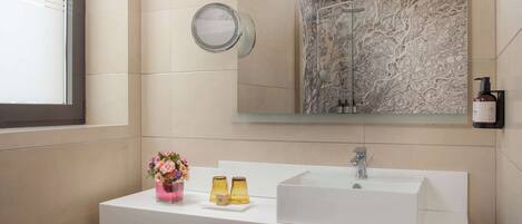 A modern bathroom with a white sink, a large mirror, and a shower with a marble wall.