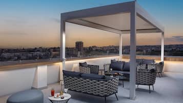 Una terrazza sul tetto con una zona salotto coperta, un bar e vista sulla città.