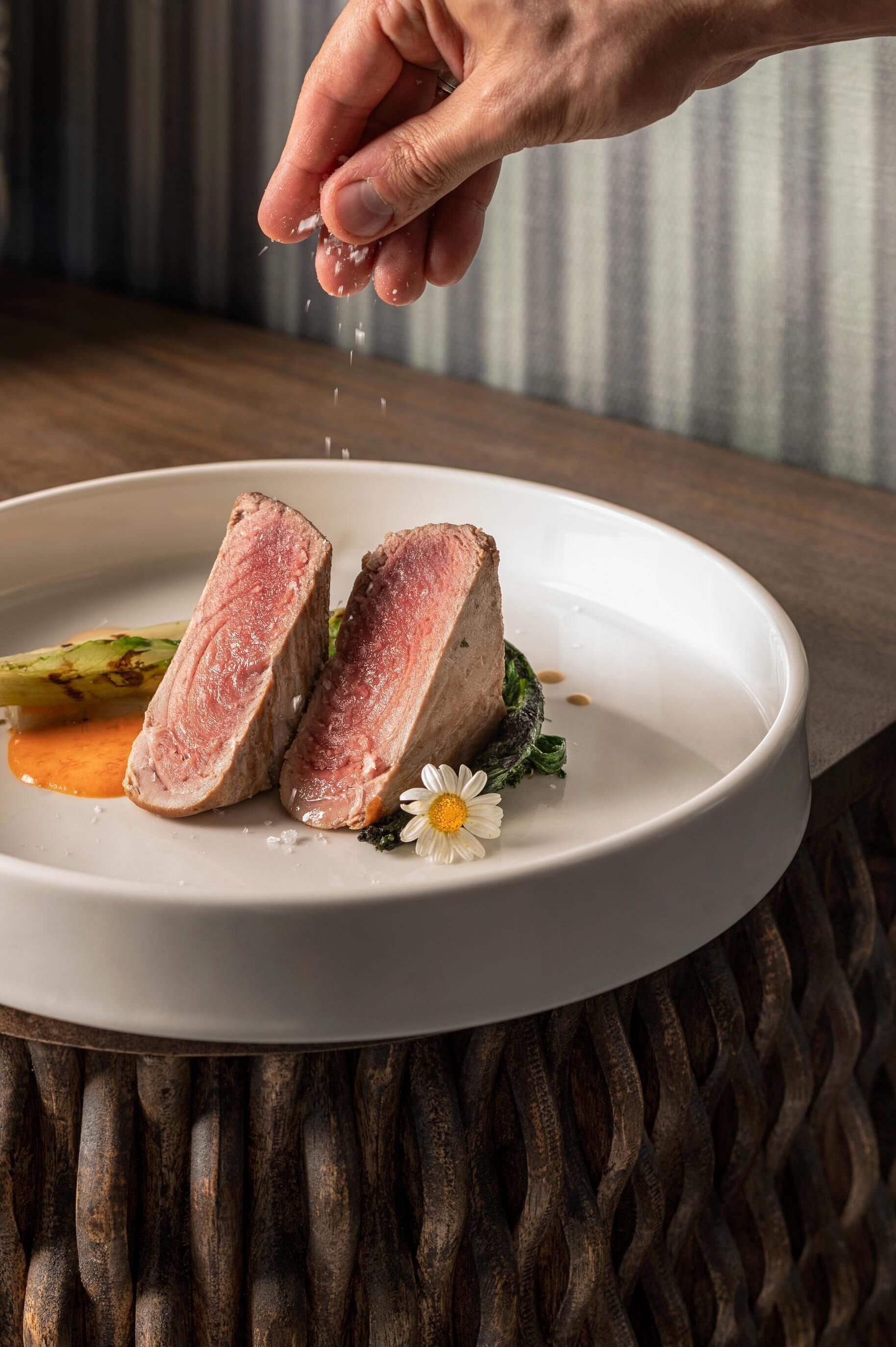 Un plato con carne cortada, verduras y una flor sobre una fuente blanca.