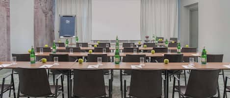 Una sala de conferencias con una larga mesa, sillas, una pantalla de proyector y botellas verdes sobre la mesa.