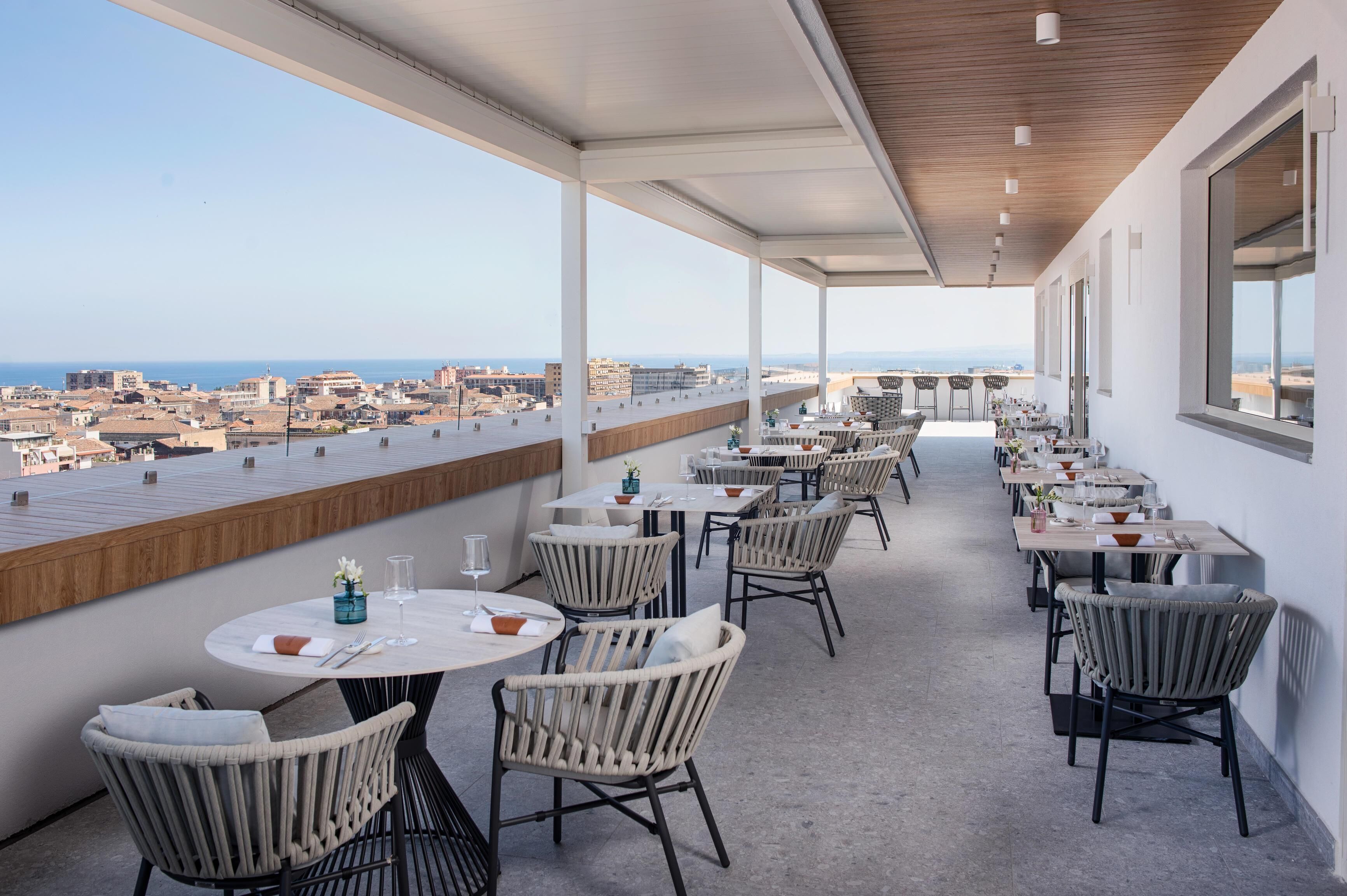 Una terraza en la azotea con mesas y sillas, que ofrece vistas a la ciudad y al mar.