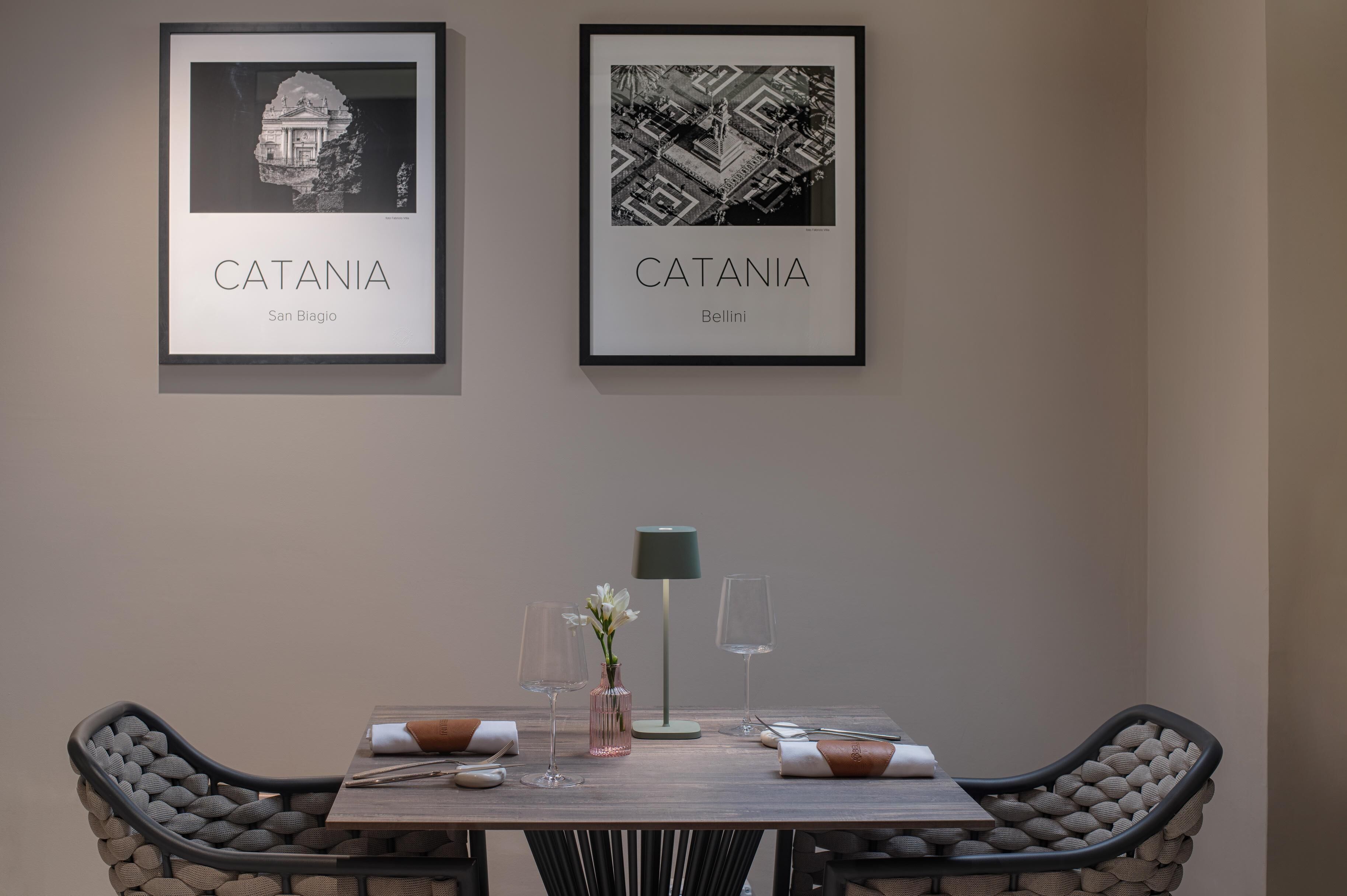 Comedor con una mesa lista para dos personas, una obra de arte enmarcada encima y una lámpara moderna sobre la mesa.