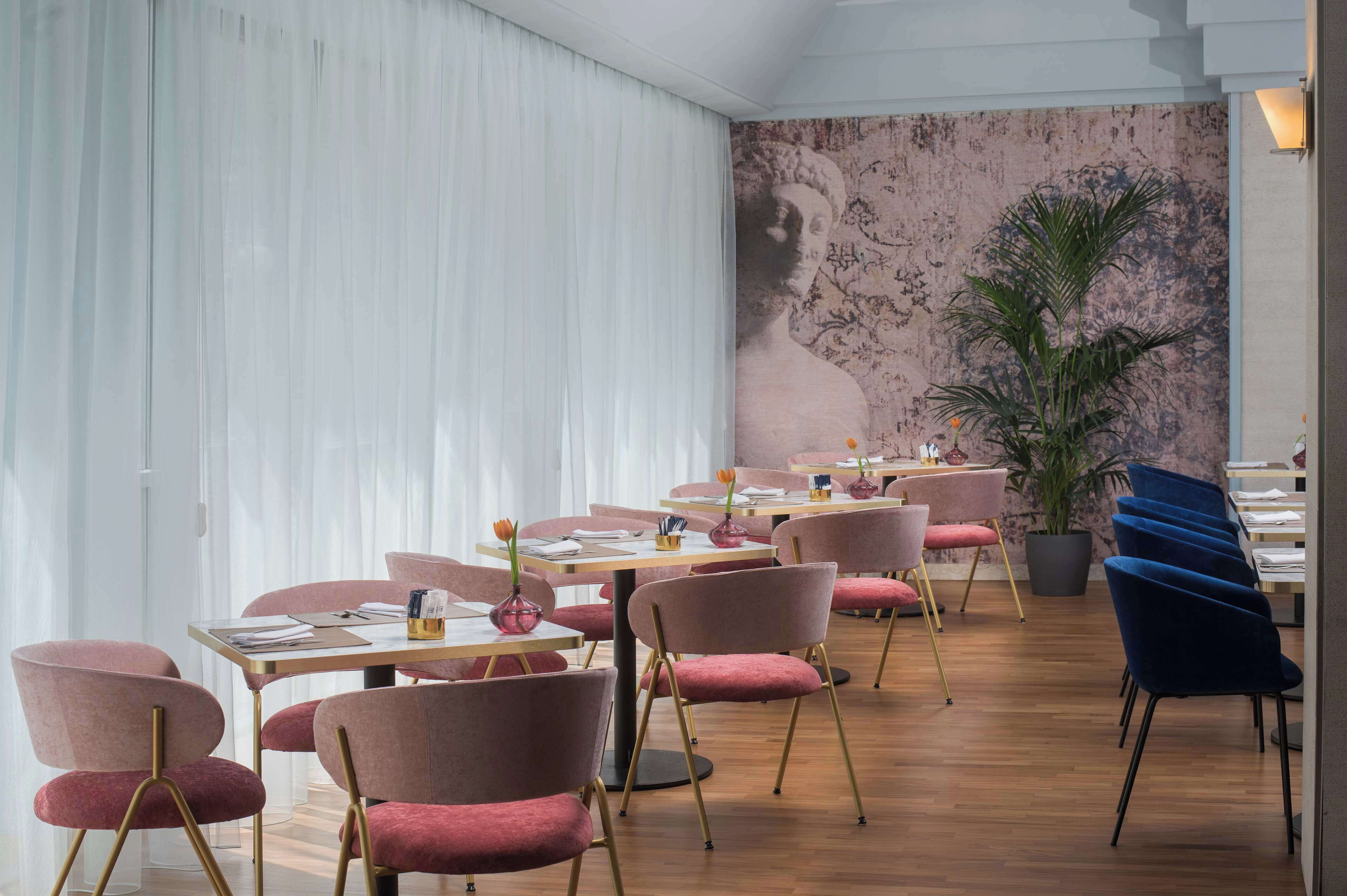 A restaurant with wooden tables and chairs, a large potted plant, and a mural on the wall.