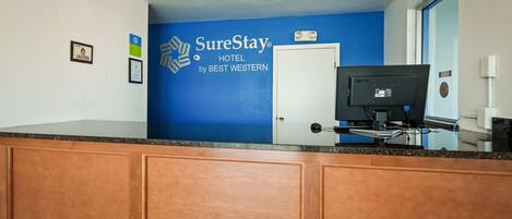 A hotel reception area with a blue wall, a SureStay logo, and a closed door.