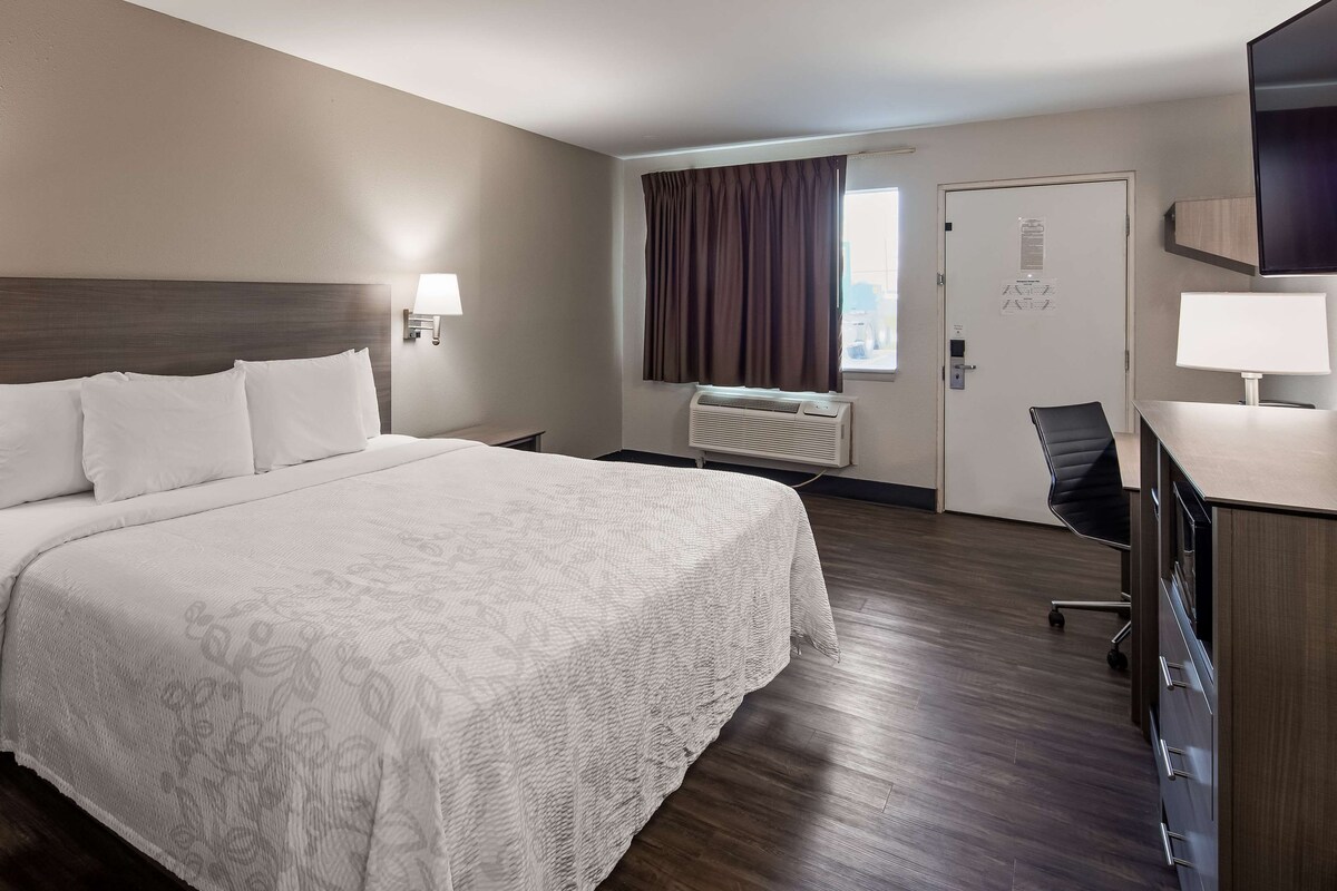 A hotel room with a large bed, two bedside lamps, a desk with a chair, a radiator, and a door with a window.
