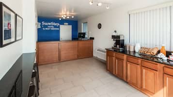 A hotel reception area with a blue wall, a SureStay sign, a coffee machine, and breakfast items on the counter.