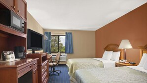 A hotel room with a desk, television, two beds, a chair, and a window with curtains.