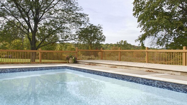 A rectangular swimming pool with a wooden deck and a fence.
