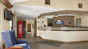 A lobby with a reception desk, a Coca-Cola refrigerator, a Day's Inn sign, and a seating area with a chair and table.