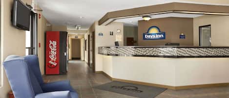 A lobby with a reception desk, a Coca-Cola refrigerator, a Day's Inn sign, and a seating area with a chair and table.
