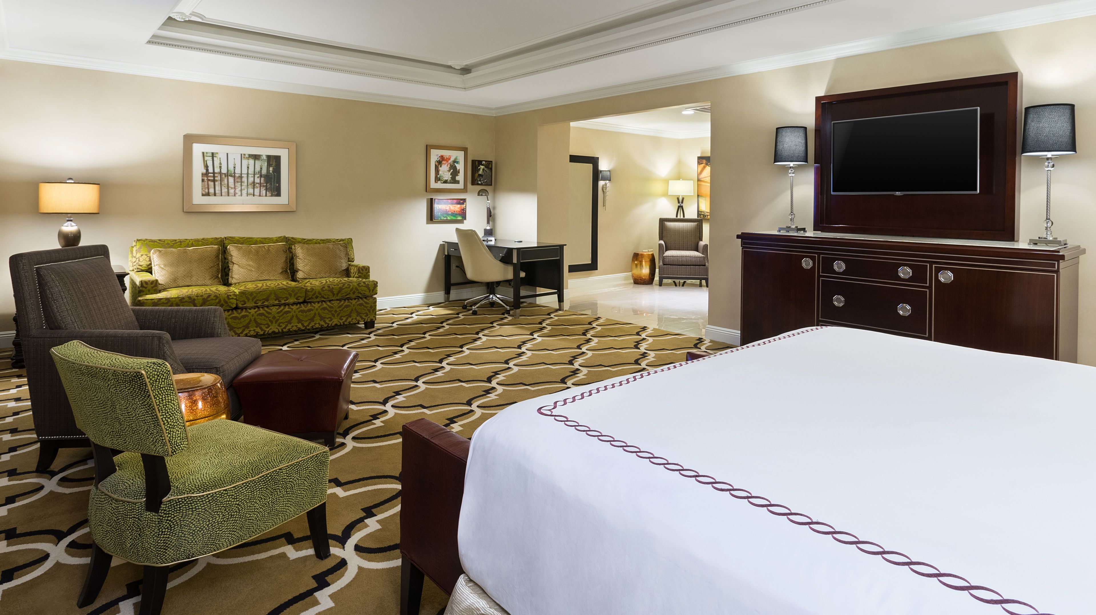 A hotel room with a large bed, a sofa, a desk, and a TV.