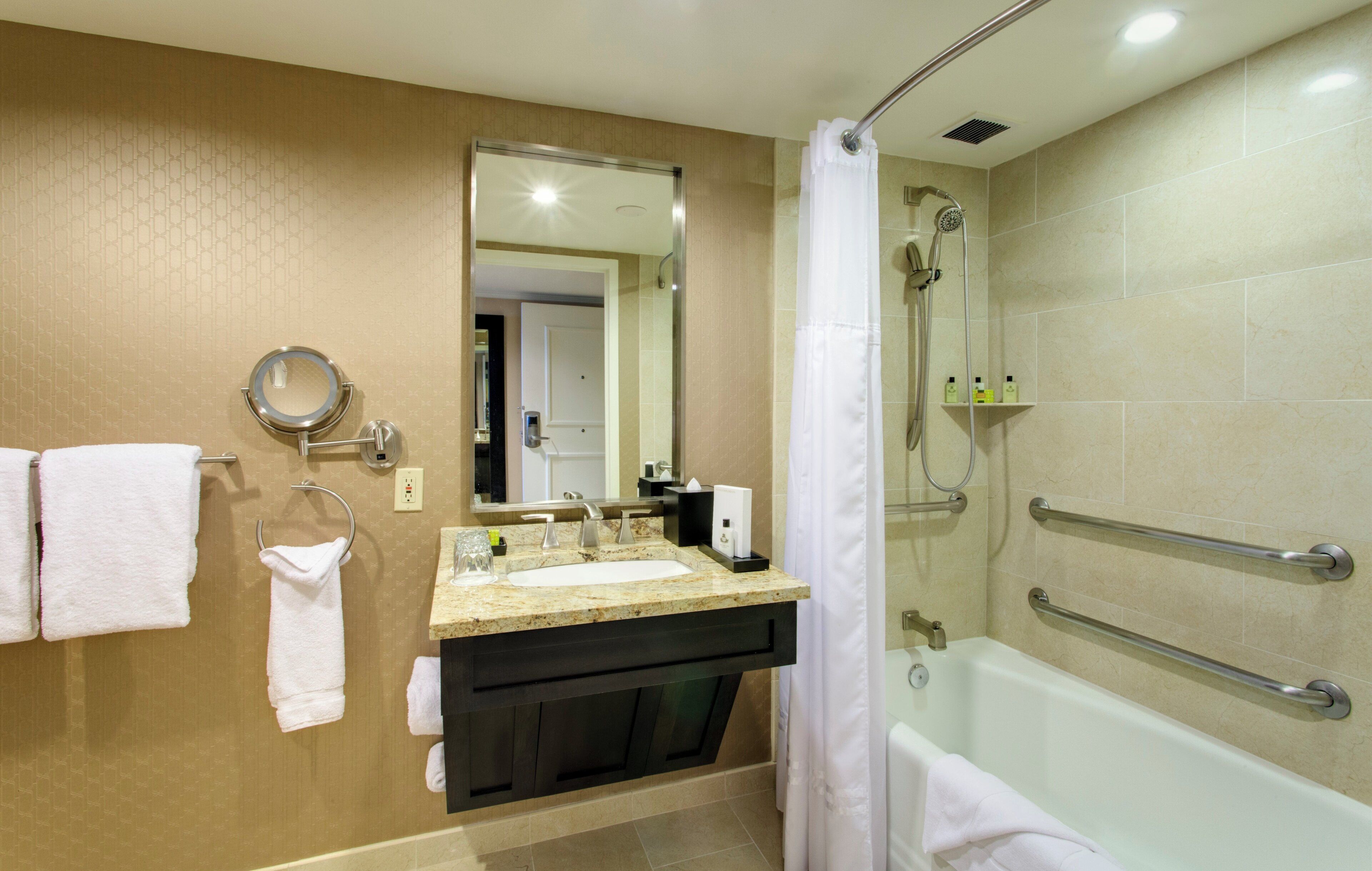 Un baño con lavamanos, espejo, toallero, ducha y barras de apoyo.