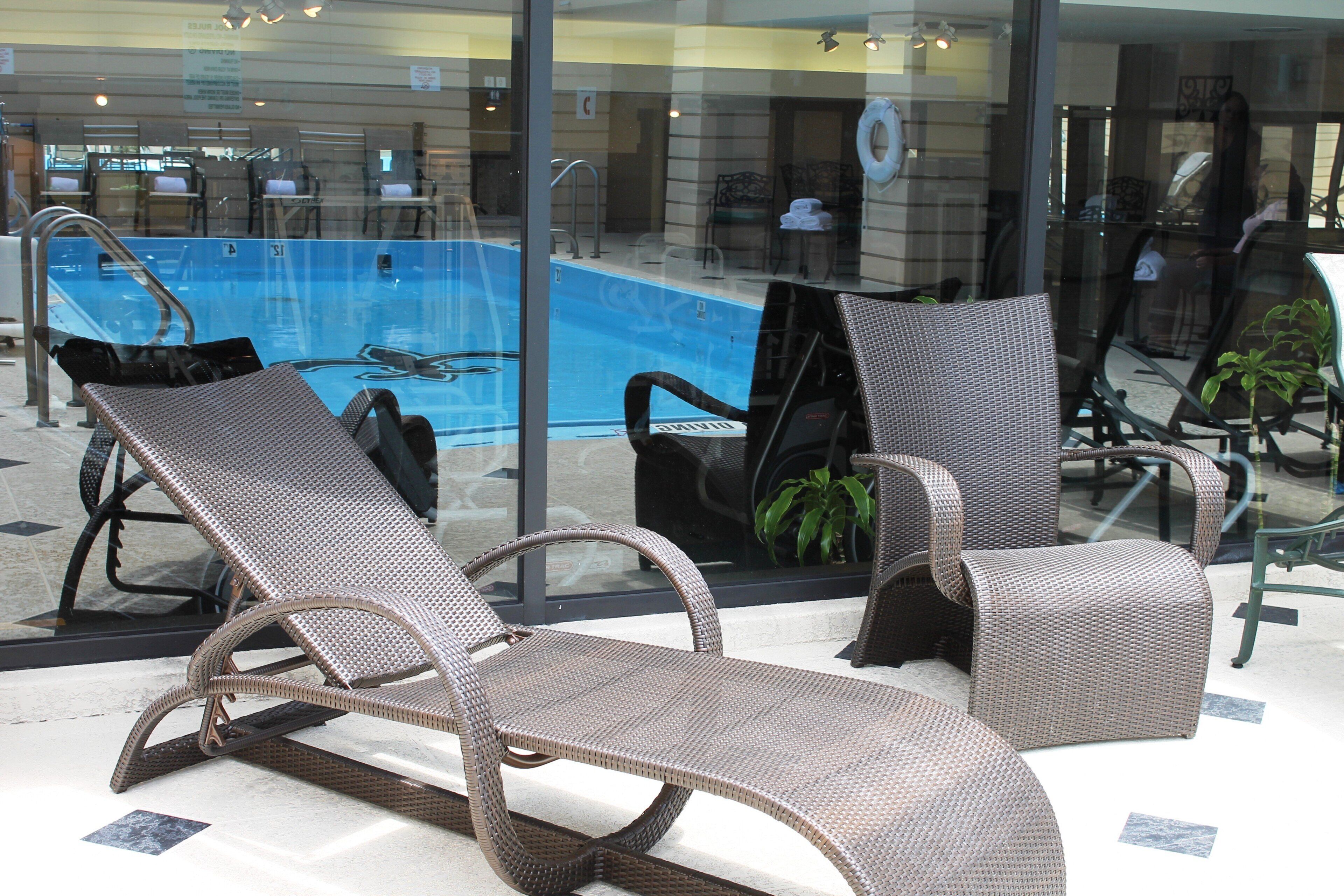 Un área junto a la piscina con sillones de mimbre y una barandilla de vidrio.