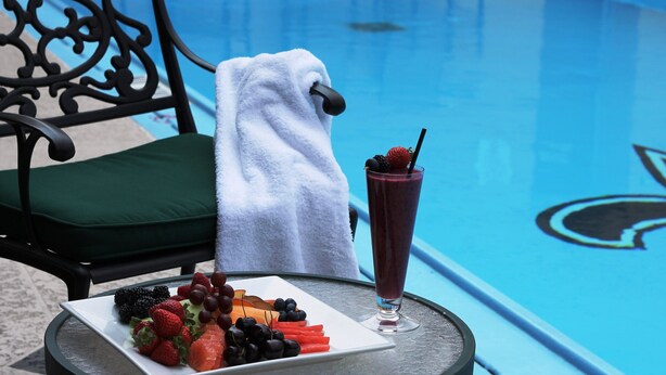 A poolside setting with a table, a plate of fruit, and a drink. - InterContinental New Orleans by IHG (New Orleans)